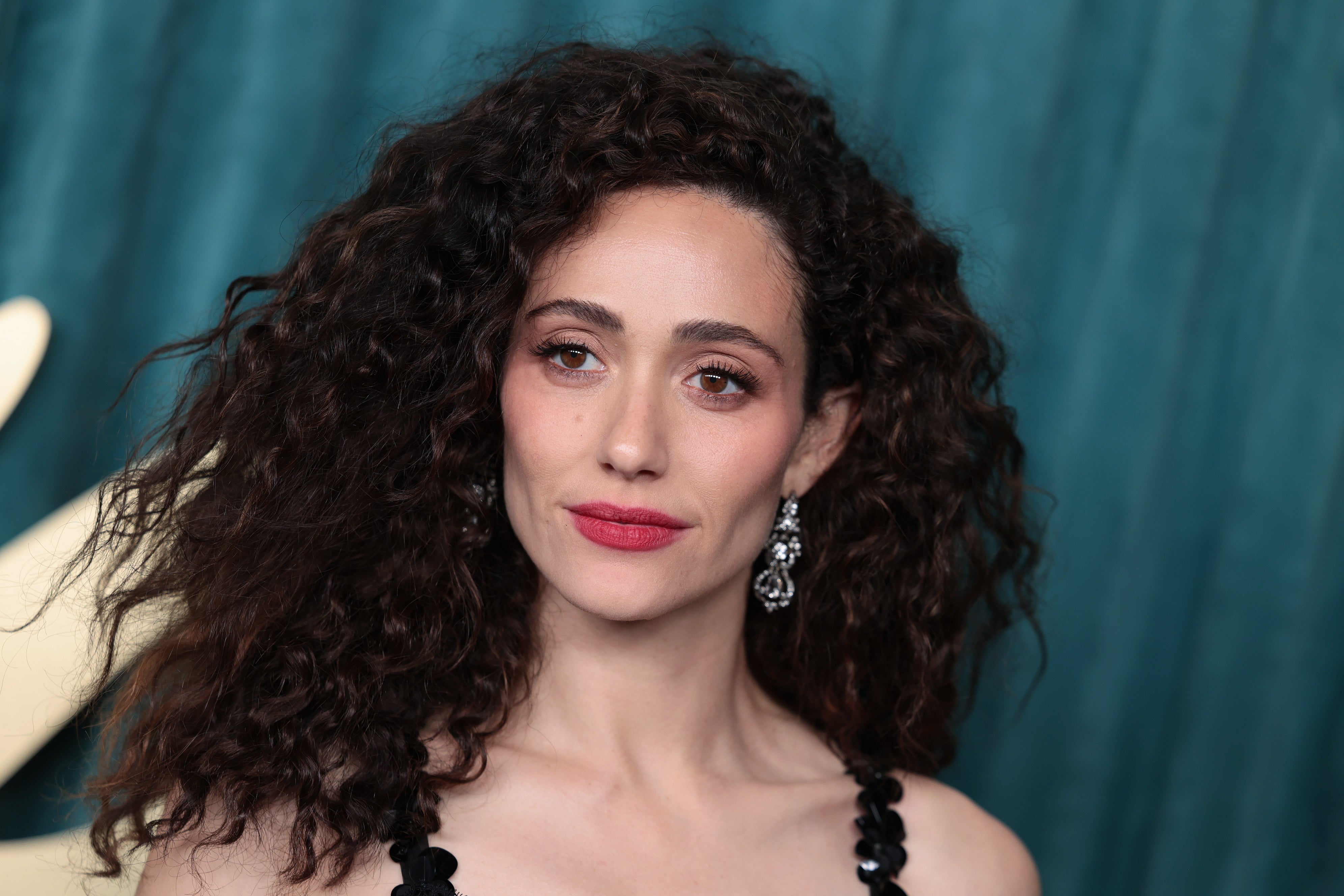 Person with curly hair and statement earrings on the red carpet, wearing a dress with textured details