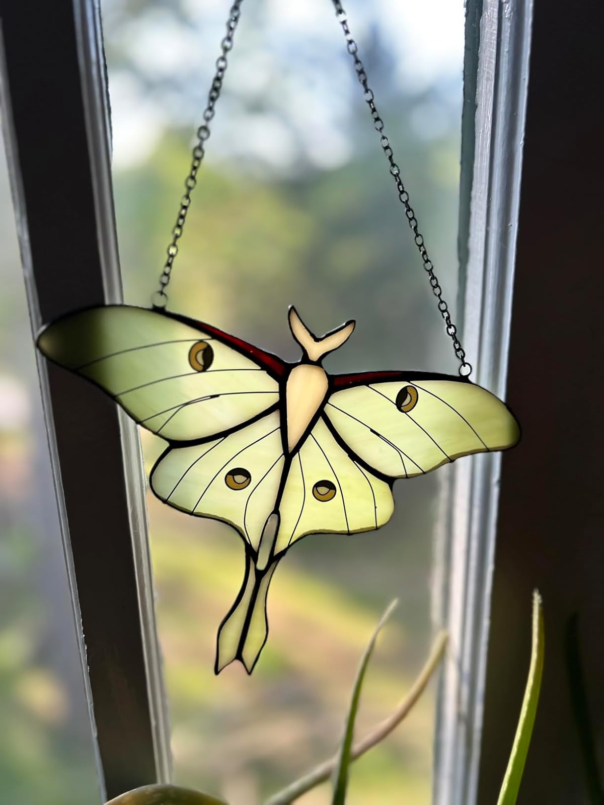 Stained glass decoration of a moth hanging by a window, showcasing delicate detailing and craftsmanship suitable for home decor
