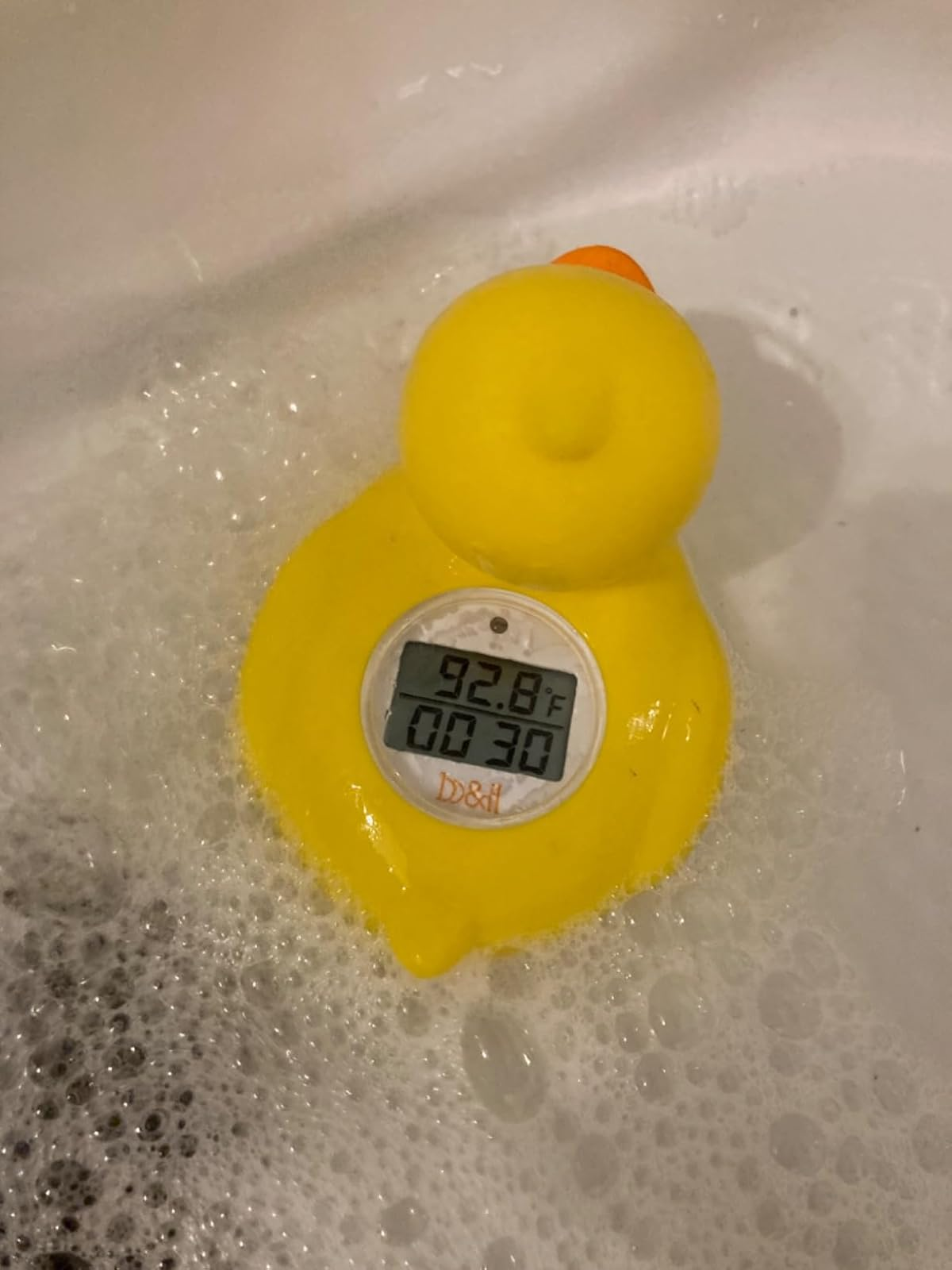 A yellow rubber duck thermometer floating in a reviewer's bubbly bath