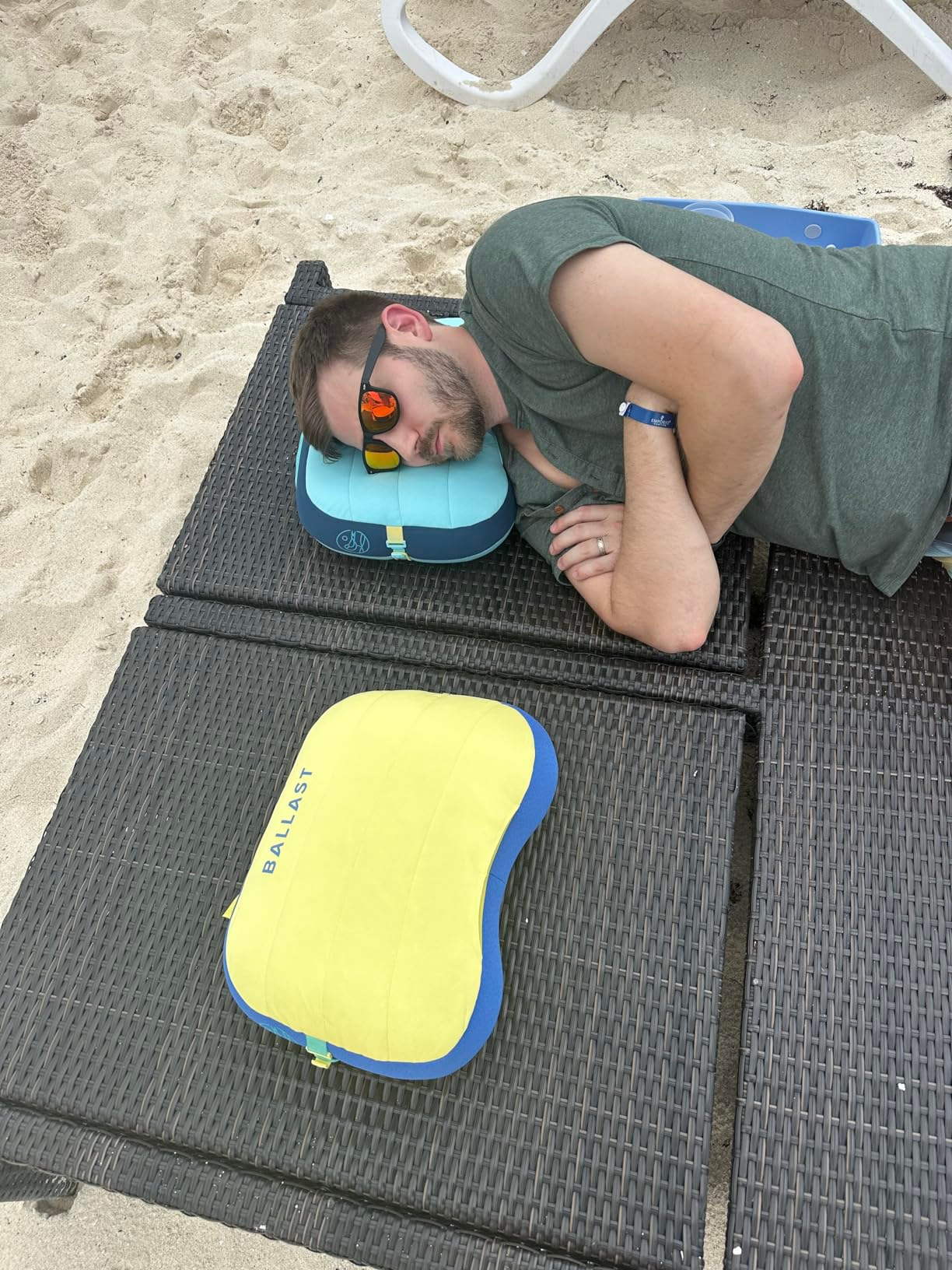 reviewer wearing sunglasses and a gray t-shirt rests on a beach chair with his head on a blue and yellow inflatable pillow labeled