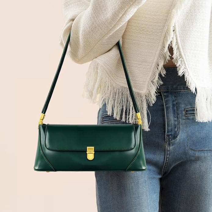 Model holding the strap of a dark green small baguette style purse with gold clasp