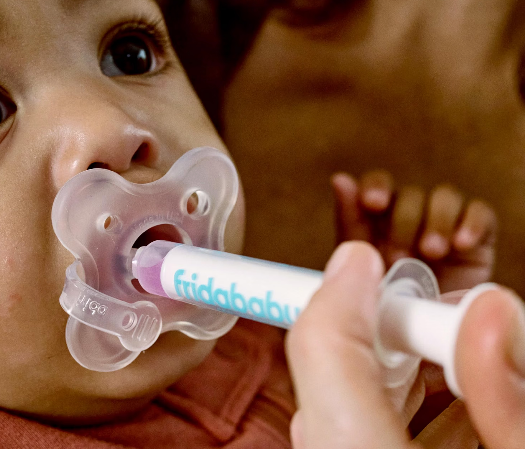 Baby using a FridaBaby pacifier medicine dispenser, calming while receiving liquid medication from a syringe