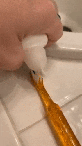 reviewer showing the white dome shaped cap on a toothpaste dispenser letting out a thin stream of toothpaste 