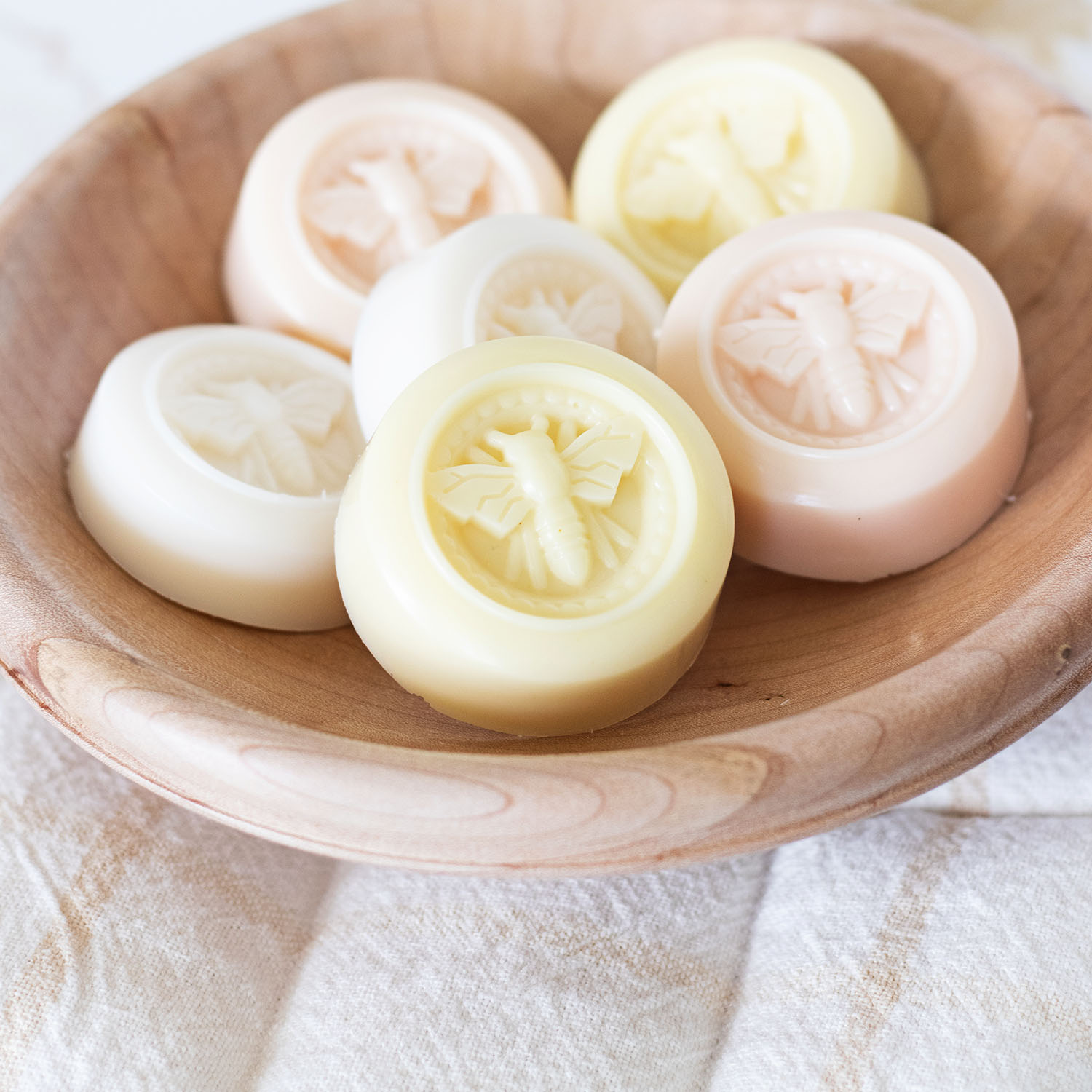 Handmade round soaps embossed with honey bees in a natural wood bowl.