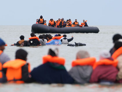 People thought to be migrants wade in the water as they attempt to board a small boat off