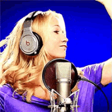 a woman wearing headphones and a purple shirt stands in front of a microphone