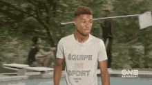 a young man wearing a white t-shirt that says equipe de sport is standing in front of a group of people .