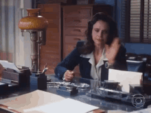 a woman is sitting at a desk with a lamp and papers