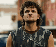 a man with curly hair is wearing a necklace with a can opener pendant