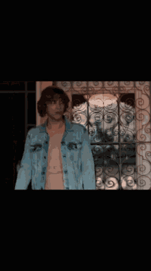a shirtless man in a denim jacket is standing in front of a door