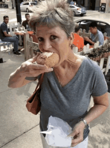 a woman in a grey shirt is eating a donut on a sidewalk