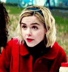 a woman wearing a red jacket and black turtleneck looks at the camera