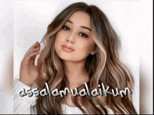 a woman with long brown hair is wearing a white sweater with the words assalamualaikum written on it .