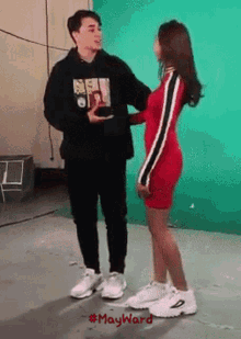 a woman in a red dress is standing next to a man wearing a black hoodie with a picture of a girl on it