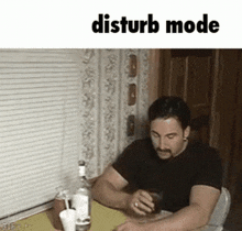 a man is sitting at a table with a drink in his hand and the words `` disturb mode '' written above him .