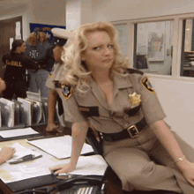 a blonde woman in a sheriff 's uniform sits at a desk