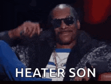 a man wearing sunglasses and a jacket is sitting in a chair with the words `` heater son '' written on the screen .