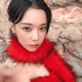 a woman wearing a red fur collar stands in front of a brick wall