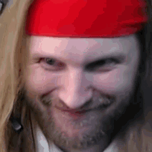 a man with a beard is wearing a red headband and smiling .