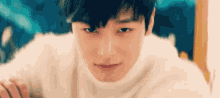a close up of a young man wearing a white sweater looking at the camera .