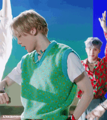 a young man wearing a green vest and a white shirt is dancing .