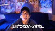 a man wearing glasses and a hat is sitting in front of a naokman show poster