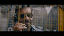 a man wearing sunglasses is talking on a phone behind bars