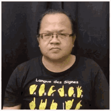 a man wearing glasses and a black t-shirt is using sign language .