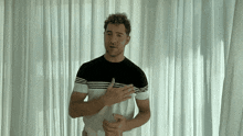 a man in a black and white striped shirt stands in front of white curtains