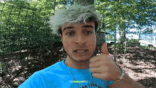a man in a blue shirt giving a thumbs up in front of trees