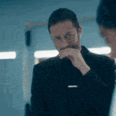 a man in a suit and tie is covering his mouth with his hand while looking at another man .