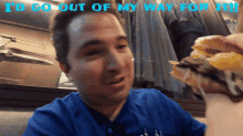 a man in a blue shirt eating a hamburger with the words " i 'd go out of my way for it " above him