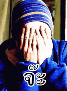 a person covering their face with their hands and a blue shirt with a foreign language written on it