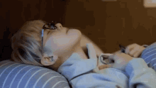 a young boy wearing glasses is laying on a bed with his eyes closed .