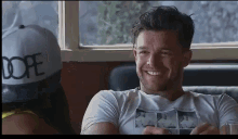 a man wearing a dope hat smiles while sitting at a table