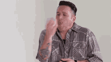 a man in a plaid shirt is blowing a kiss while standing in front of a white wall .