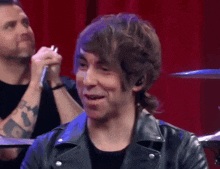 a man in a black leather jacket is smiling in front of a drum set