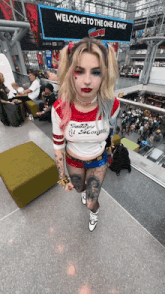 a woman in a harley quinn costume stands in front of a welcome to the one and only sign