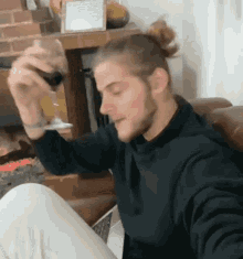 a man in a black sweater is sitting on a couch holding a glass of wine