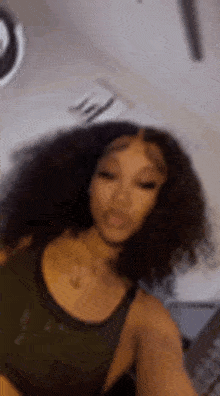 a woman with curly hair is taking a selfie while wearing a green tank top .