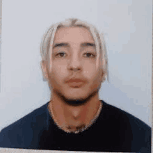 a man with blonde hair is wearing a black shirt and a gold chain around his neck .