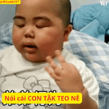 a baby is laying on a bed with a yellow sticker that says " noi cai con tak teo ne "