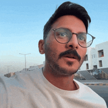 a man with glasses and a beard is standing in front of a building