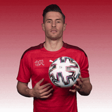 a man in a red shirt is holding a soccer ball in his hands