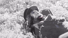a black and white photo of a man laying in a field of flowers
