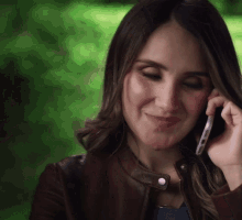 a woman wearing a brown leather jacket is talking on a cell phone