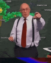 a man in a white shirt and red tie is pointing at the camera in front of a weather map