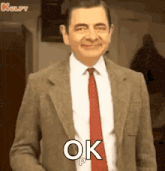 mr bean is wearing a suit and tie and is smiling and saying ok .