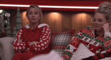 two women sitting on a couch with their arms crossed wearing christmas sweaters