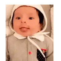 a baby wearing a white hat and a gray shirt is sticking his tongue out .